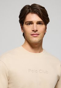 Beige långärmad skjorta med ett präglat "Polo Club"-logotyp på bröstet. Tyget verkar slätt med en regular fit och rundad halsdesign.