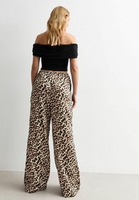 Schwarzes, schulterfreies Oberteil kombiniert mit weit geschnittenen, leopardenmusterigen Hosen. Die Hosen haben einen lockeren Sitz und einen elastischen Bund. Weiche Stofftextur.