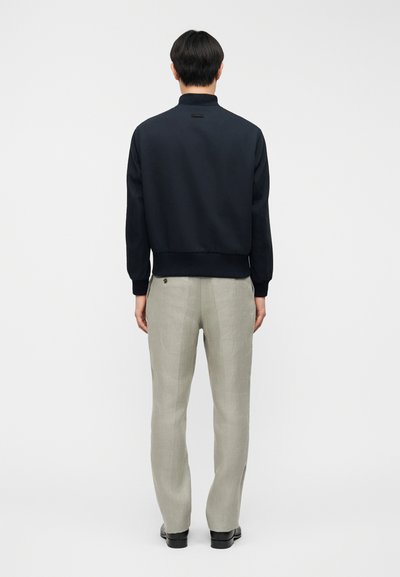 Πουλόβερ σε ναυτικό μπλε με ψηλό γιακά και ριμπ τελείωμα, συνδυασμένο με ανοιχτό γκρι παντελόνια λινό με λεπτομέρεια κουμπιού στην πίσω τσέπη.