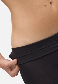 Leggings negros de punto con una suave cinturilla elástica. La cinturilla está ligeramente doblada, revelando una textura de piel suave y clara debajo.