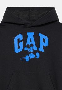 Felpa nera con testo blu "GAP" e una grafica di Topolino seduto sulla parte anteriore, dotata di tasca frontale e rivestimento interno del cappuccio.