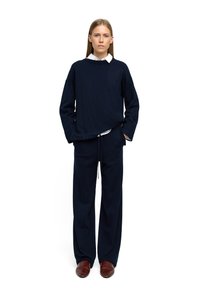 Granatowy sweter dzianinowy z okrągłym dekoltem, w połączeniu z szerokimi granatowymi spodniami. Stylizacja zawiera białą koszulę z kołnierzykiem pod spodem. Brązowe buty.