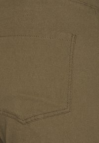 Olivgröna tyg med en bakficka med en sydd kant och en mjuk textur. Subtila nyansvariationer i materialet.