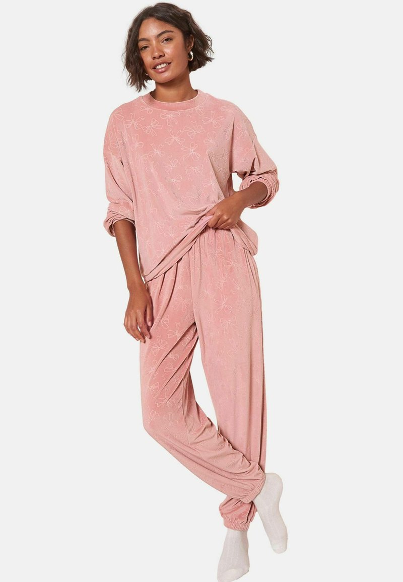 Conjunto de ropa de estar por casa en rosa, con una camisa de manga larga con estampado y pantalones ajustados. Tejido suave, corte relajado, con detalles florales.