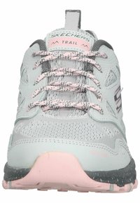 zapatillas de trail gris claro con acentos rosas, parte superior de malla texturizada, cordones grises y cordones con patrón. Suela de goma con un ligero borde rosa.