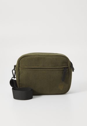 Green corduroy bag with a zippered main compartment, front pocket, and a black strap. Features textured fabric and minimal hardware detailing.