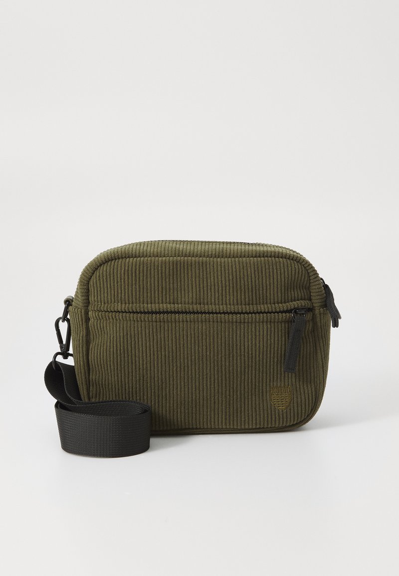 Grønne kordfløjl taske med et lynlåset hovedrum, frontlomme og en sort rem. Har struktureret stof og minimal hardwaredetaljering.