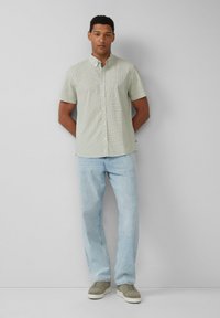 Kurzärmliges, grün kariertes Hemd mit Knopfschluss, kombiniert mit hellblauen, geraden Jeans und olivgrünen Sneakers.