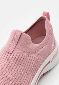 Zapatilla Skechers Go Walk rosa con parte superior de tejido texturizado, cuello elástico y una entresuela blanca con acentos rosas. Diseño suave y ligero.