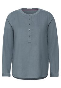 Maglietta azzurra a maniche lunghe con scollatura rotonda, placket a tre bottoni e orlo leggermente curvo. Realizzata in un morbido tessuto testurizzato.