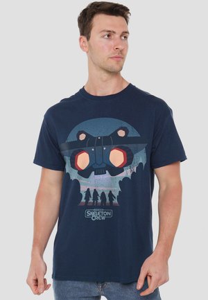 Navy blue cotton t-shirt featuring a graphic print of a helmeted figure with bright orange accents and silhouetted characters below.