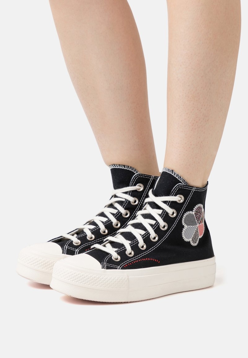 Schwarze Canvas High-Top-Sneaker mit weißen Gummisohlen, versehen mit gesticktem Kleeblatt-Muster und weißen Schnürsenkeln. Strukturierte Zehenkappe und seitliche Nähte.