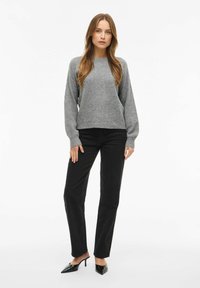 Maglione grigio a maglia testurizzata con scollatura rotonda e maniche lunghe abbinato a pantaloni neri a gamba dritta e tacchi a punta neri.