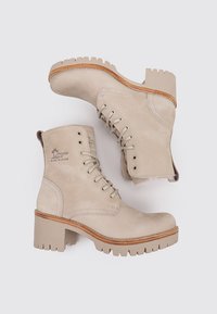 Beige Lederstiefeletten mit runder Zehenform, Schnürung vorne und dickem, robustem Absatz. Merkmale sind die kontrastierende braune Sohle und dezente Markenkennzeichnung.