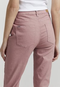 Pantalones de algodón rosa con un diseño de pierna recta. Cuenta con dos bolsillos traseros, detalles de costura y una pequeña etiqueta de la marca cerca de la cinturilla.