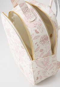 Zaino con motivo floreale in un morbido bianco e rosa chiaro; presenta cerniere dorate e doppi scomparti con una forma strutturata e una superficie texturizzata.