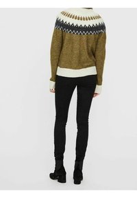 Pull en laine avec un col de couleur claire et un empiècement à motifs en gris foncé et blanc, associé à un jean slim noir et des bottines.