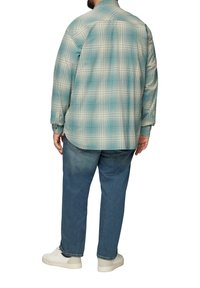 Niebieska i kremowa koszula w kratkę wykonana z lekkiego materiału, z długimi rękawami, karczkiem z tyłu i zapinanymi na guziki mankietami, noszona z dżinsowymi spodniami i trampkami.