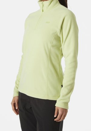 Woman wearing a light green long-sleeve fleece pullover with a front zipper and black pants, standing against a plain background.