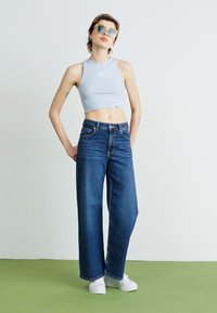 Blue denim wide-leg jeans with a high waist, paired with a light blue cropped top. Model wears sunglasses and white sneakers.