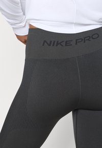 Čierne legíny Nike Pro s hladkou, elastickou tkaninou. Obsahujú široký pás so zvýšeným logom a textúrované rebrované akcenty pozdĺž stehien.