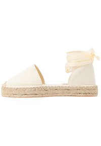 Espadrille en toile blanc cassé avec une semelle en jute et de doux liens en ruban autour de la cheville. Présente un bout pointu et des côtés ouverts.