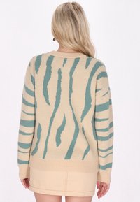 Maglione beige con strisce astratte teal, polsini e orlo a coste, realizzato in tessuto a maglia testurizzata. Design casual con vestibilità rilassata.