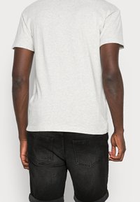 Grå bomulds T-shirt med korte ærmer, lige snit og ensfarvet ryg; parret med sort denim jeans med fem lommer.