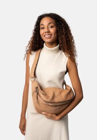 Borsa a spalla in pelle color cuoio con forma curvata, chiusura con zip e tracolla regolabile. Texture liscia e dettagli sottili sulla parte anteriore.