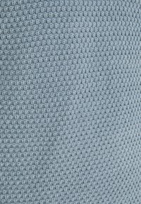 Tissu tricoté bleu clair présentant un motif tissé texturé avec de petits carrés en relief, offrant une finition douce et tactile.