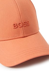 Casquette de baseball en tissu orange corail avec un logo brodé "BOSS" de couleur assortie. Comprend un bord structuré et des accents de couture.