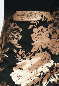 Μαύρο ύφασμα με μεταλλικό σχέδιο λουλουδιών σε ροζ χρυσό με υφή. Η μέση είναι επίσης μεταλλική, ενισχύοντας την οπτική αντίθεση.