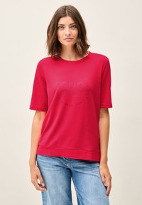 T-shirt en coton rouge à manches courtes, avec un design circulaire imprimé en bleu avec le texte "Sono Felice." Coupe décontractée, style simple.