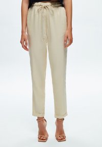 Pantalon beige à cordon de serrage avec une coupe décontractée, chevilles retroussées et tissu léger. Doté d'un lien décoratif avec des accents en bois.