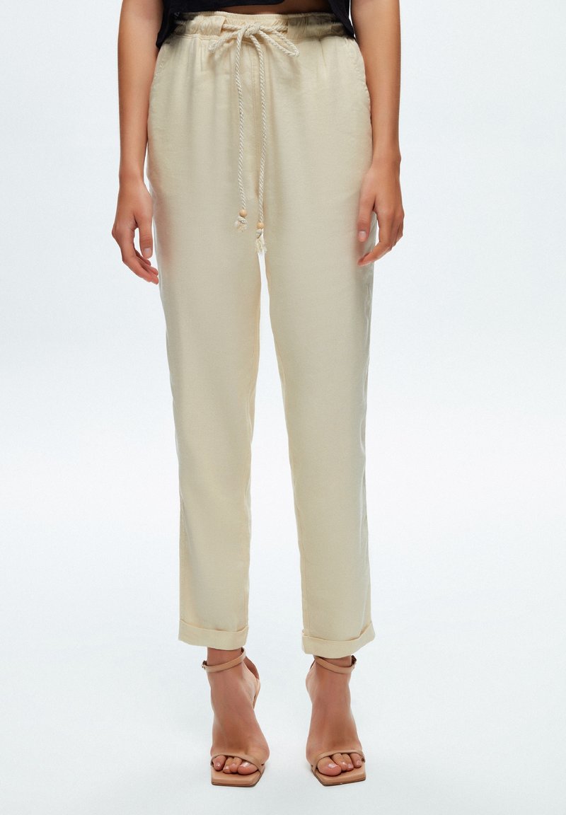 Pantalon beige à cordon de serrage avec une coupe décontractée, chevilles retroussées et tissu léger. Doté d'un lien décoratif avec des accents en bois.