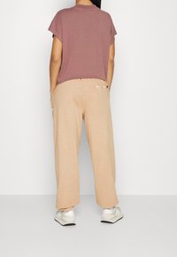 Kortärmad, mauve topp i kombination med beige, lösa byxor. Byxorna har sidofickor och en mjuk textur, loungas med vita skor.