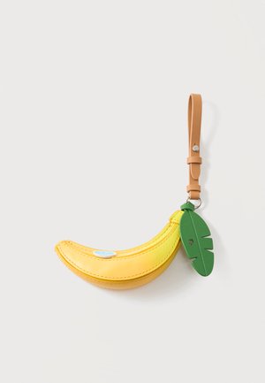 Žlté kožené puzdro v tvare banánu so zeleným príveskom listu a béžovým remienkom na zápästie na jednoduchom pozadí.