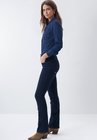 Mørkeblå denimskjorte med brystlommer og knaplukning, parret med mørke flared jeans og brune ruskindsankelstøvler.