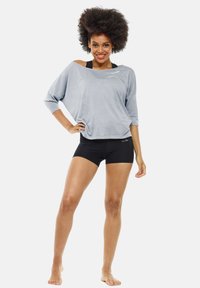 Lichtgrijze losse top met driekwart mouwen en schouderuitsnijding, gecombineerd met zwarte shorts. Soepele textuur; minimale branding.