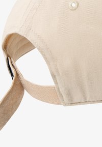 Ανοιχτό μπεζ καπέλο με δομημένη κορώνα, ραμμένες λεπτομέρειες και μαλακό ρυθμιζόμενο λουράκι στο πίσω μέρος. Ύφασμα με λεία υφή.