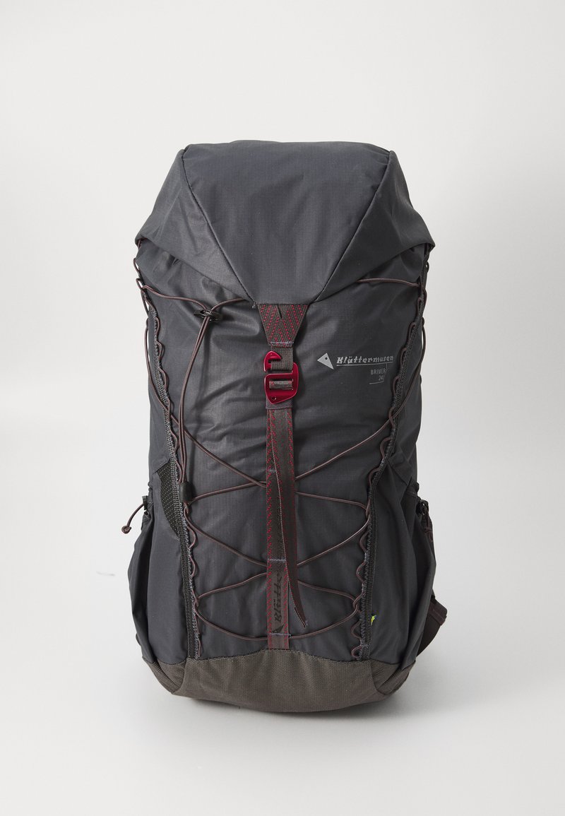 Dunkelgrauer Rucksack mit strukturierter Oberfläche, verstellbaren Trägern, roten Akzenten und einem Zugverschluss. Seitentaschen und ein markiertes Logo sind vorhanden.