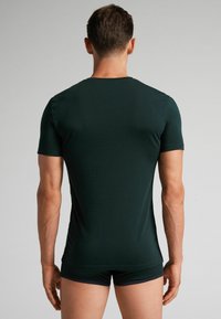 Ciemnozielona koszulka z krótkim rękawem wykonana z miękkiego materiału, dopasowany krój, gładka tekstura i okrągły dekolt, noszona z dopasowanymi szortami.