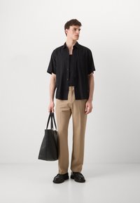 Camicetta nera a maniche corte, pantaloni beige, borsa nera con manici e scarpe nere. Texture liscia, design casual, con dettagli minimi.