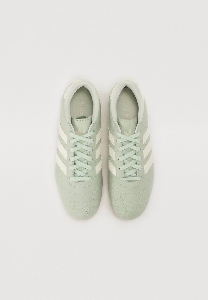Zapatillas de cuero verde claro con tres rayas blancas, cordones planos y cuello acolchado. Presentan detalles cosidos y una textura suave.
