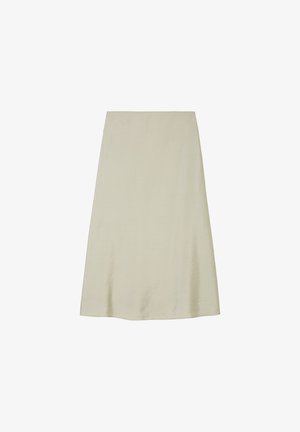 Femme portant une robe midi sans manches beige clair à fines bretelles et des mocassins blancs sans lacets, debout sur un sol neutre devant un mur uni.