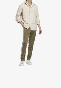 Ljusbeige linneskjorta med uppvikta ärmar, kombinerad med olivgröna avsmalnande byxor med vita sidostripes och vita sneakers.