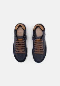 Zapatillas navy con una mezcla de tela suave y perforada, detalles en marrón y cordones marrones. Cuenta con un cuello acolchado y una plantilla acolchada.