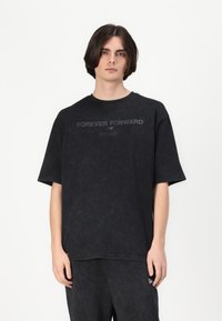 Black oversized t-shirt in a soft, textured fabric features a subtle print "FOREVER FORWARD" and "EST 1965" on the front.