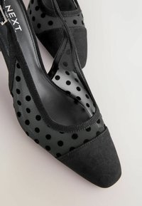 Czarny but na wysokim obcasie zamszowy, z zaostrzonym noskiem, bokami wykonanymi z siateczki ozdobionej czarnymi welurowymi groszkami oraz gładką, zakrzywioną sylwetką.