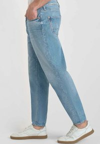 Jeans in denim azzurro chiaro con taglio dritto e cuciture visibili. Indossati con sneakers bianche con suole in gomma marrone.